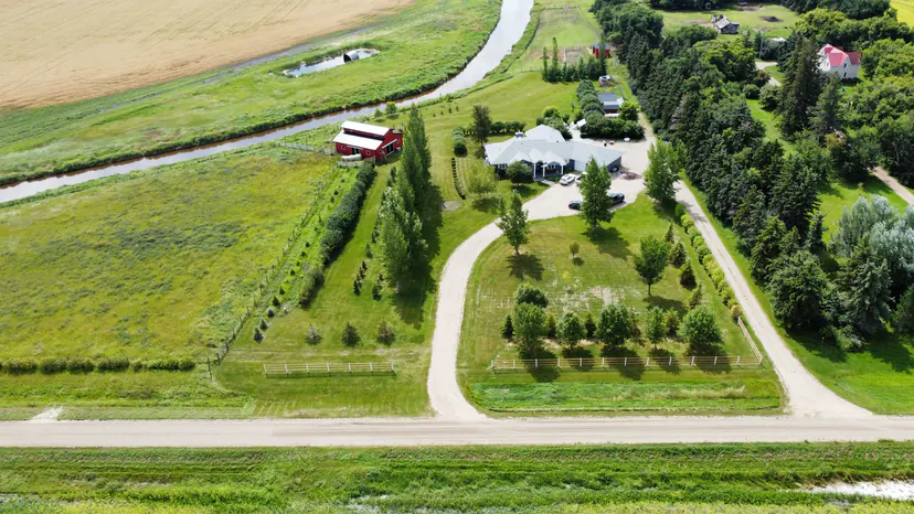 The whole property from the grid road: curved gravel drive, white rail fences, poplar rows, the house, the red barn, the creek and wheat fields.