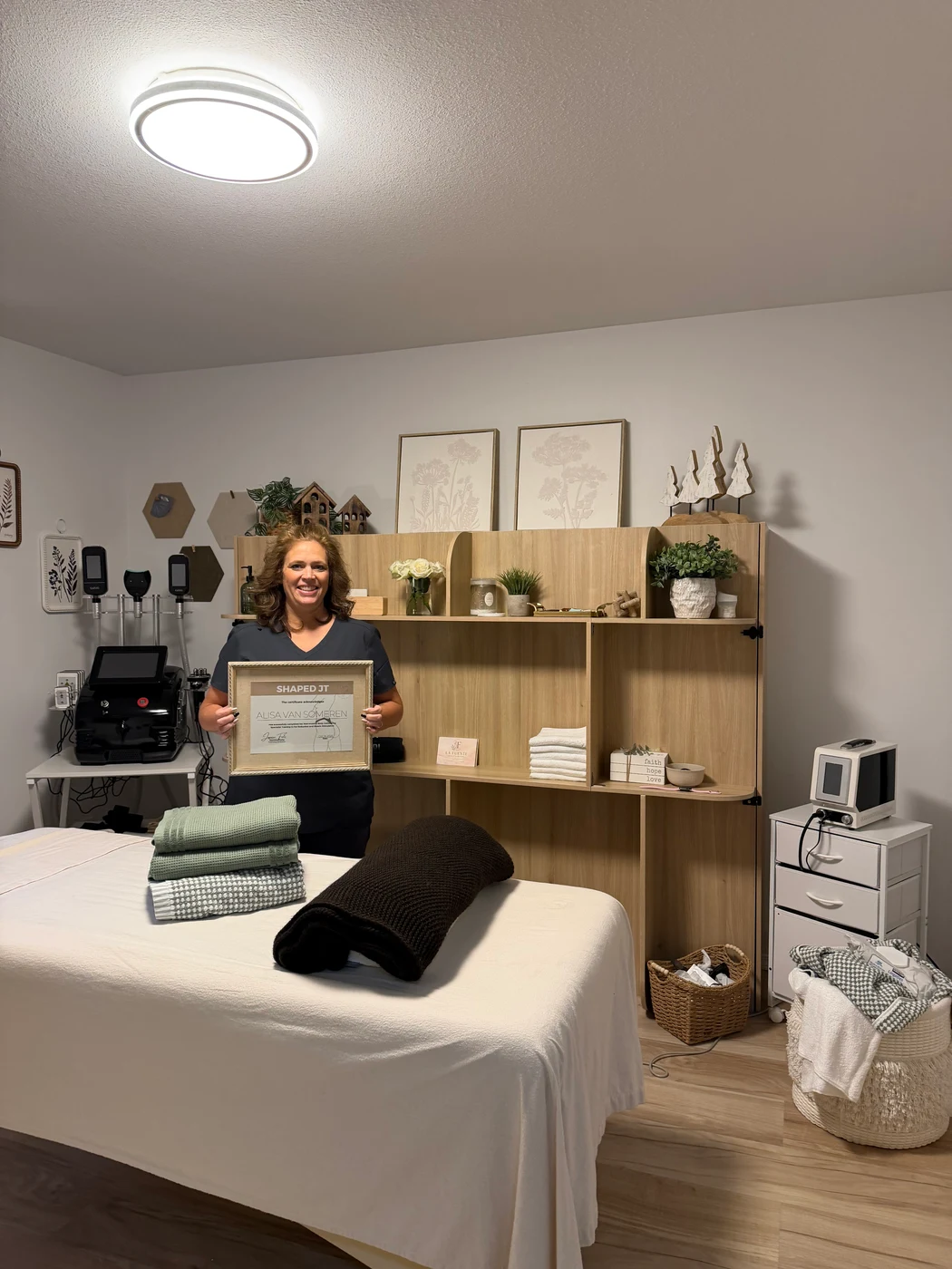 Alisa holding her body-contouring certification in her treatment studio at La Fuente Escapes.