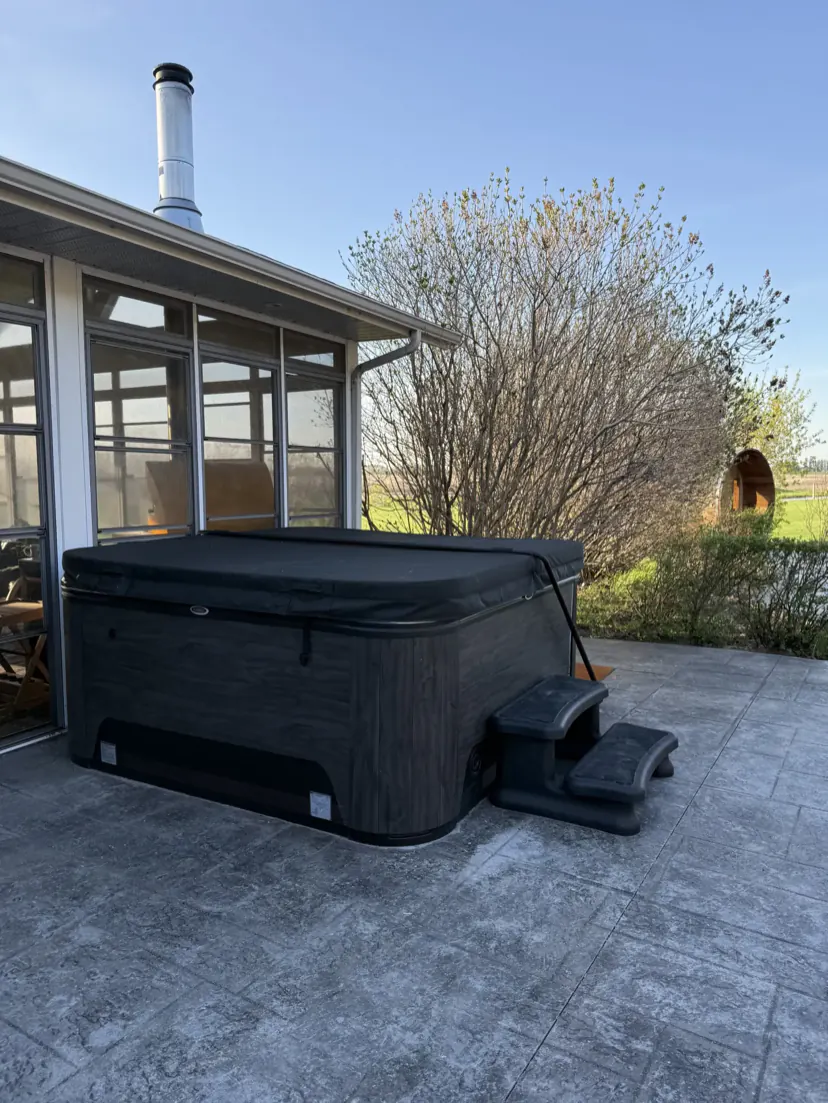 The covered hot tub on the stamped-concrete patio beside the sunroom, under a clear blue sky.