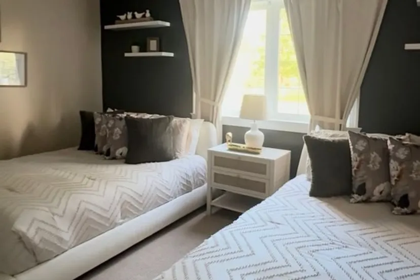 The Prairie Suite: two white upholstered queen beds with textured white bedding and floral pillows, beside a curtained window against a black feature wall.