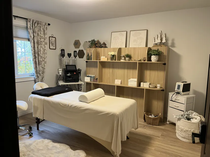The same room set up as my spa: a treatment table with white linens, a contouring device by the window, and the wooden wall cabinet the bed folds into.
